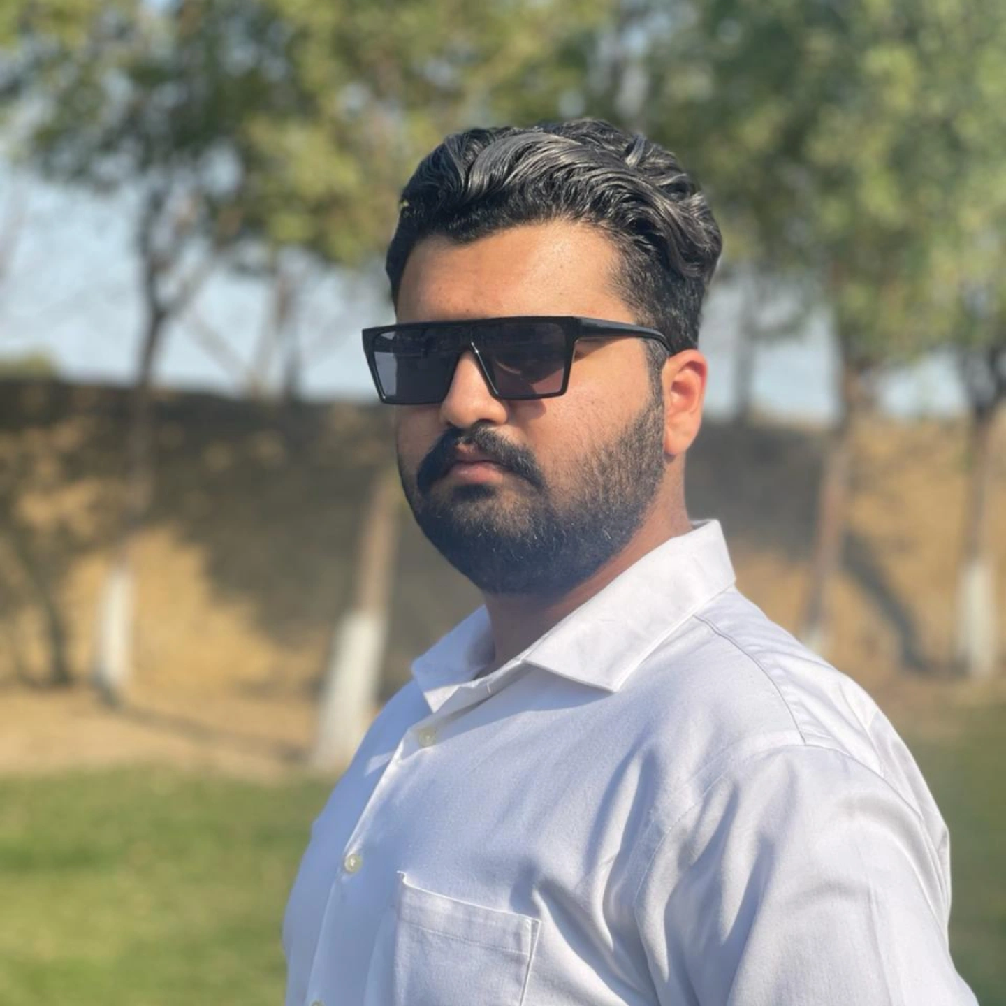 Portrait of Ali Laal Shahbaz wearing black sunglasses and a white shirt outdoors.